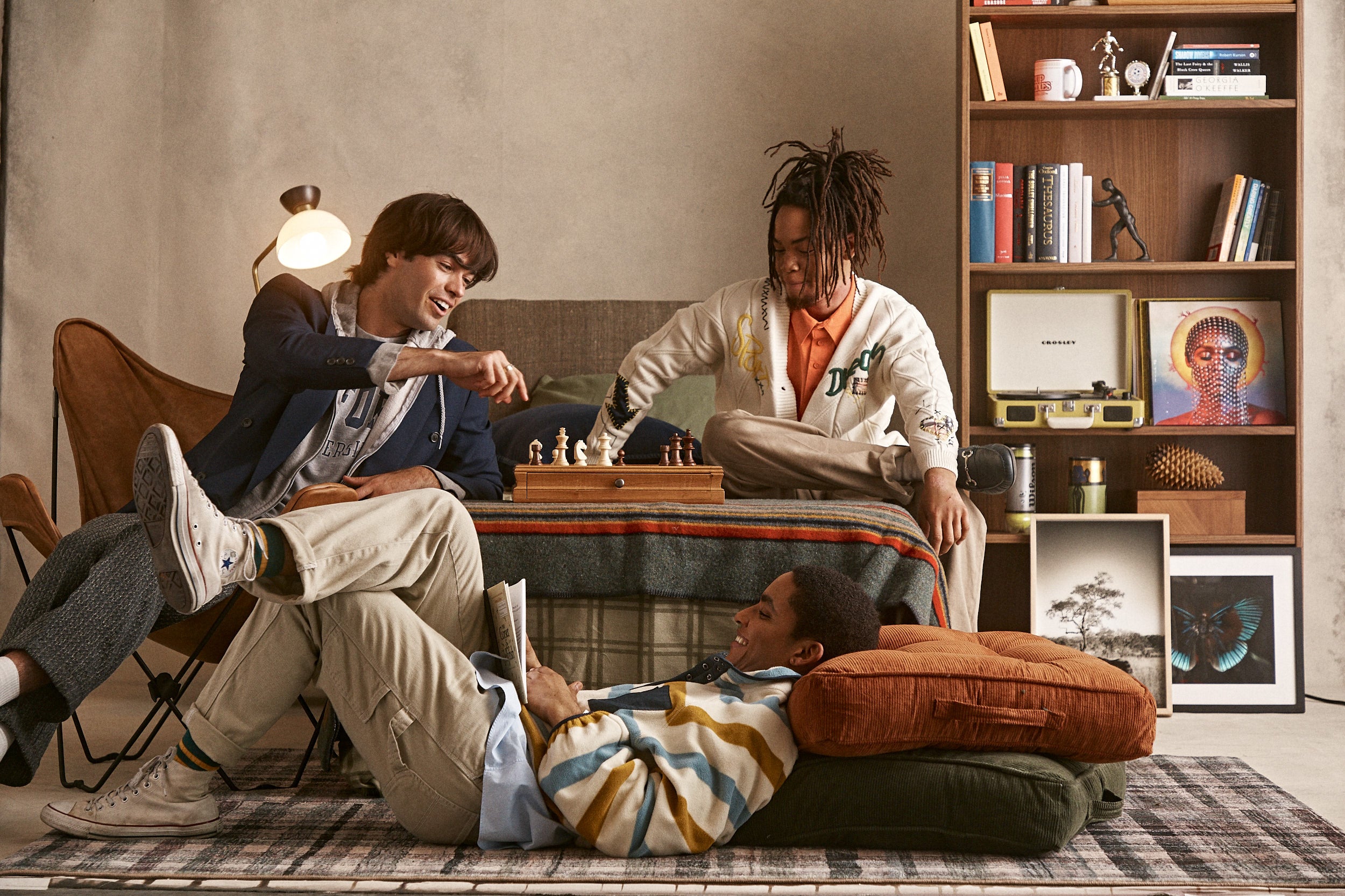 Three people sitting on a couch in a cozy living room with a bookshelf and decorative items