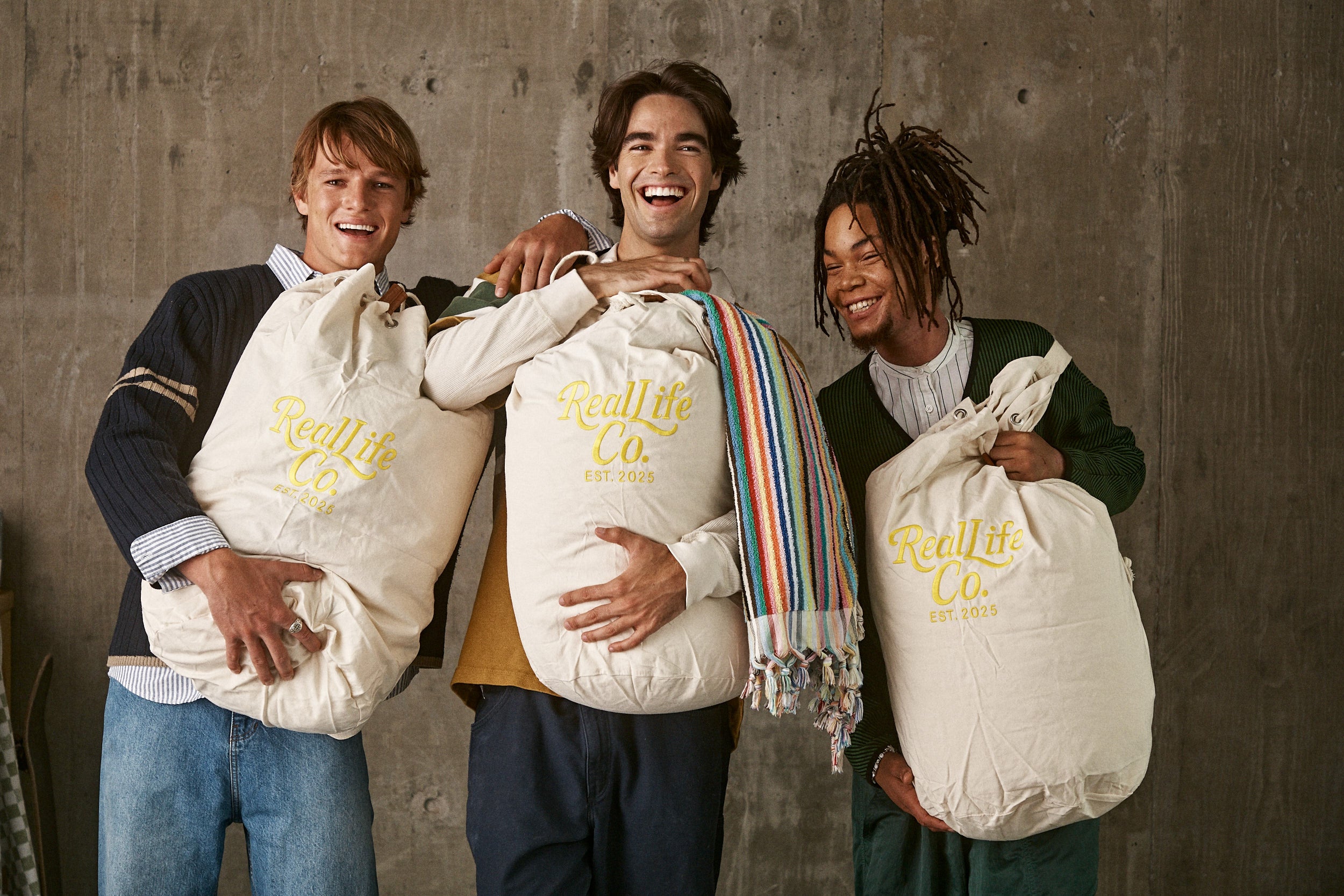 Three people holding bags with 'Wellth Co.' branding against a concrete wall.